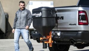 Man walking behind pickup truck with salt spreader attachment